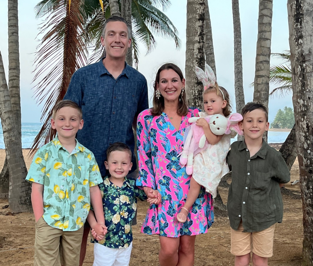 Cunningham with her husband and four children standing on a beach with palm trees behind them.